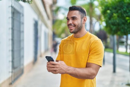 Photo pour Jeune homme hispanique souriant confiant en utilisant un smartphone dans la rue - image libre de droit