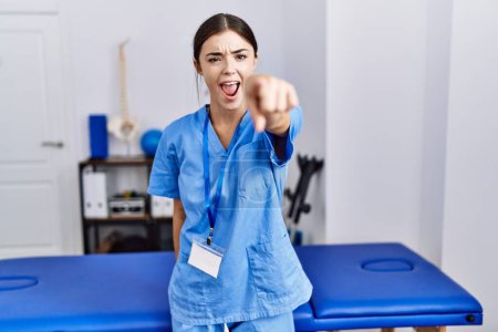 Photo for Young hispanic woman wearing physiotherapist uniform standing at clinic pointing displeased and frustrated to the camera, angry and furious with you - Royalty Free Image