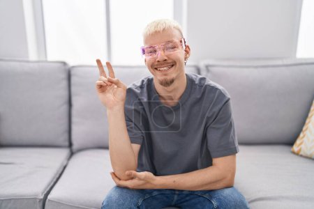 Photo for Young caucasian man wearing virtual reality glasses smiling with happy face winking at the camera doing victory sign. number two. - Royalty Free Image
