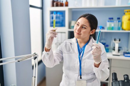 Photo for Young hispanic woman wearing scientist uniform holding test tubes at laboratory - Royalty Free Image