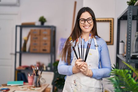 Téléchargez les photos : Young woman artist smiling confident holding paintbrushes at art studio - en image libre de droit