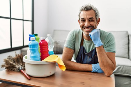 Foto de Hombre de pelo gris de mediana edad sonriendo confiado apoyado en la mesa en casa - Imagen libre de derechos