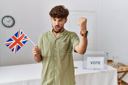 Foto de Joven árabe en las elecciones de campaña política con bandera del Reino Unido molesto y frustrado gritando con ira, gritando loco de ira y la mano levantada - Imagen libre de derechos