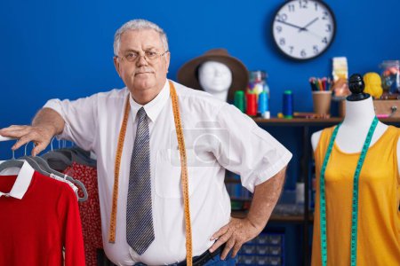 Photo for Middle age grey-haired man tailor leaning on clothes rack at tailor shop - Royalty Free Image