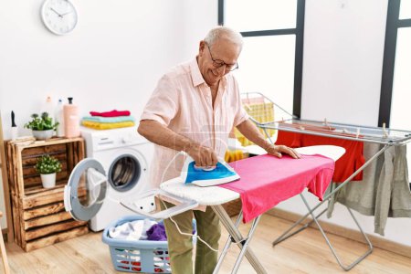 Téléchargez les photos : Senior man smiling confident ironing clothes at laundry room - en image libre de droit
