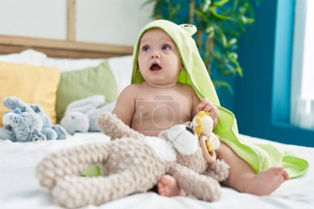 Foto de Adorable bebé caucásico usando una toalla divertida jugando con juguetes en el dormitorio - Imagen libre de derechos