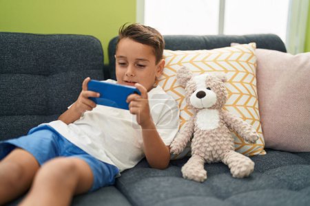 Photo for Adorable hispanic toddler playing video game lying on sofa at home - Royalty Free Image