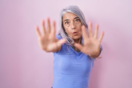 Photo for Middle age woman with tattoos standing over pink background afraid and terrified with fear expression stop gesture with hands, shouting in shock. panic concept. - Royalty Free Image