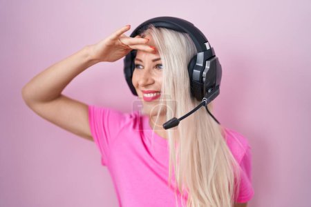Photo for Caucasian woman listening to music using headphones very happy and smiling looking far away with hand over head. searching concept. - Royalty Free Image