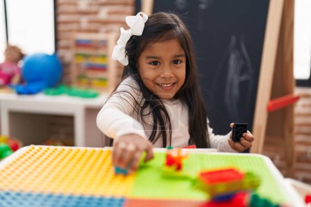 Téléchargez les photos : Adorable fille hispanique jouant avec des blocs de construction assis sur la table à la maternelle - en image libre de droit