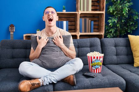 Photo for Young man eating popcorn angry and mad screaming frustrated and furious, shouting with anger looking up. - Royalty Free Image