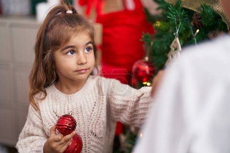 Foto de Adorable chica hispana decorando árbol de navidad en casa - Imagen libre de derechos