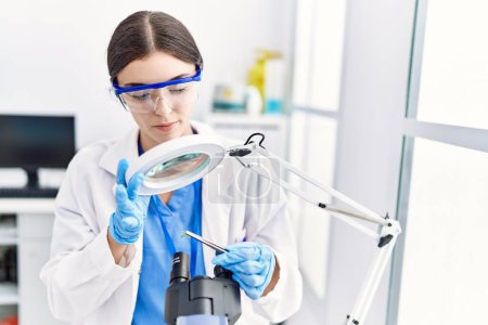 Photo for Young hispanic woman wearing scientist uniform analysing insect at laboratory - Royalty Free Image