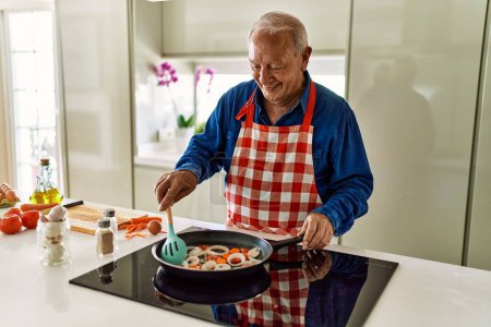 Foto de Hombre mayor sonriendo confiado cocinar en la cocina - Imagen libre de derechos