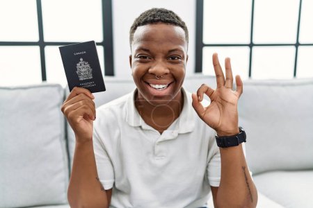 Foto de Joven africano portador de pasaporte canada haciendo ok signo con los dedos, sonriendo gesto amistoso excelente símbolo - Imagen libre de derechos