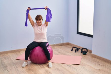 Photo for Middle age woman smiling confident stretching arm using elastic band at sport center - Royalty Free Image