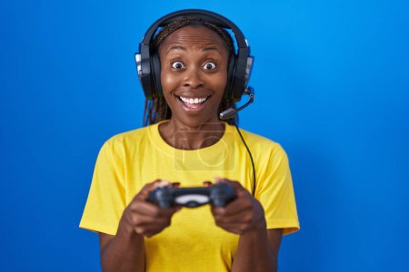 Foto de Mujer afroamericana jugando videojuegos celebrando loco y sorprendido por el éxito con los ojos abiertos gritando emocionado. - Imagen libre de derechos