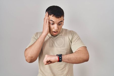 Foto de Hombre árabe joven con camiseta casual mirando el tiempo del reloj preocupado, con miedo de llegar tarde - Imagen libre de derechos