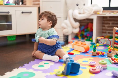 Photo for Adorable hispanic toddler sitting on floor with serious expression playing at kindergarten - Royalty Free Image