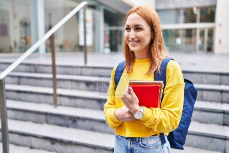 Téléchargez les photos : Jeune étudiante caucasienne souriante confiante tenant des livres à l'université - en image libre de droit