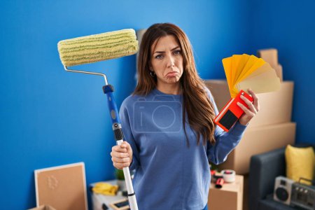 Photo for Young brunette woman holding roller painter painting new house depressed and worry for distress, crying angry and afraid. sad expression. - Royalty Free Image