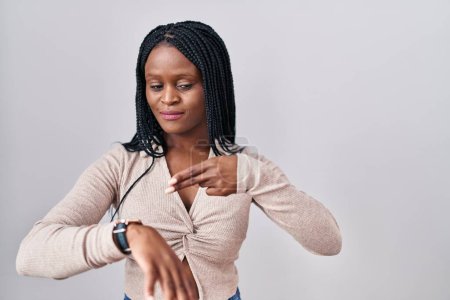 Téléchargez les photos : Femme africaine avec des tresses debout sur fond blanc à la hâte pointant pour regarder le temps, l'impatience, bouleversé et en colère pour retard de délai - en image libre de droit