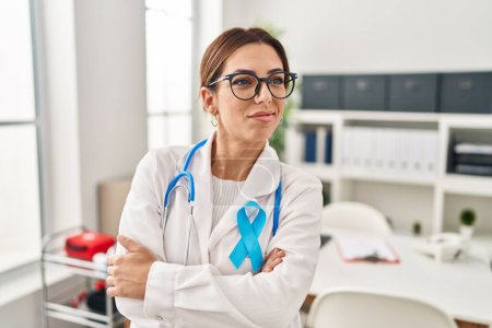 Téléchargez les photos : Jeune femme brune médecin portant stéthoscope à la clinique souriant regardant vers le côté et regardant loin en pensant. - en image libre de droit