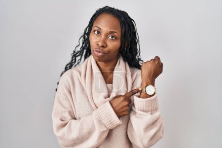 Téléchargez les photos : Femme africaine debout sur fond blanc à la hâte pointant vers regarder le temps, l'impatience, regardant la caméra avec une expression détendue - en image libre de droit