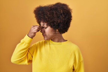 Foto de Mujer afroamericana joven de pie sobre fondo amarillo cansada frotando nariz y ojos sintiendo fatiga y dolor de cabeza. concepto de estrés y frustración. - Imagen libre de derechos
