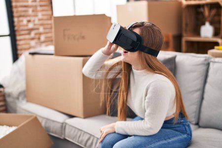 Téléchargez les photos : Jeune femme blonde utilisant des lunettes de réalité virtuelle assis sur le canapé à la nouvelle maison - en image libre de droit