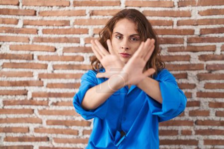 Photo for Beautiful brunette woman standing over bricks wall rejection expression crossing arms and palms doing negative sign, angry face - Royalty Free Image
