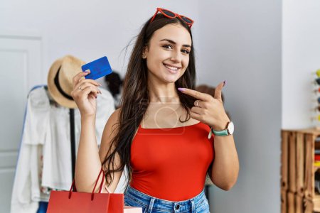 Téléchargez les photos : Jeune femme brune tenant des sacs à provisions et carte de crédit souriant heureux pointant avec la main et le doigt - en image libre de droit