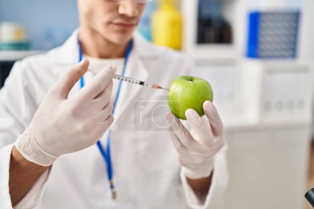 Téléchargez les photos : Young hispanic man wearing scientist uniform injecting on apple at laboratory - en image libre de droit