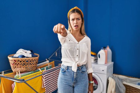 Photo for Young blonde woman at laundry room pointing displeased and frustrated to the camera, angry and furious with you - Royalty Free Image