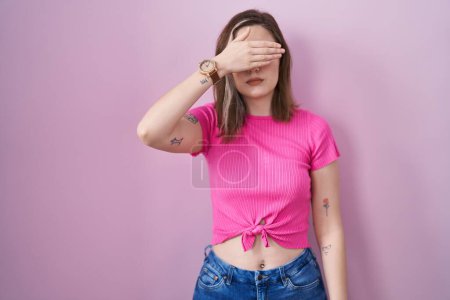 Photo for Blonde caucasian woman standing over pink background covering eyes with hand, looking serious and sad. sightless, hiding and rejection concept - Royalty Free Image