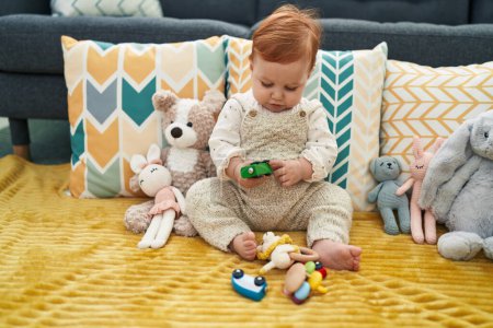 Photo for Adorable redhead toddler playing with car toy sitting on sofa at home - Royalty Free Image