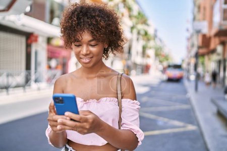 Téléchargez les photos : Jeune fille afro-américaine souriant heureux en utilisant un smartphone à la ville. - en image libre de droit