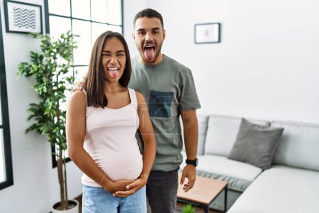 Téléchargez les photos : Jeune couple interracial attend un bébé, toucher ventre enceinte langue collante heureux avec une expression drôle. concept d'émotion. - en image libre de droit