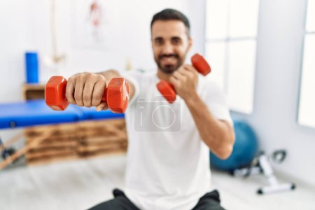 Photo for Young hispanic man patient smiling confident having rehab session boxing using dumbbells at clinic - Royalty Free Image