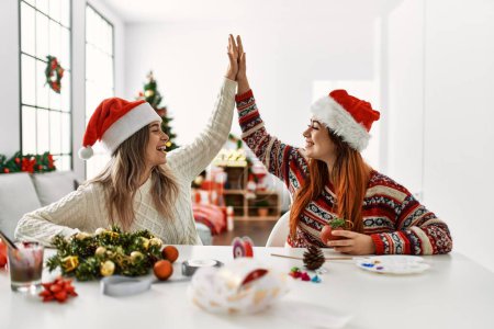 Foto de Mujer pareja haciendo hecho a mano la decoración de Navidad alta cinco levantó las manos en casa - Imagen libre de derechos