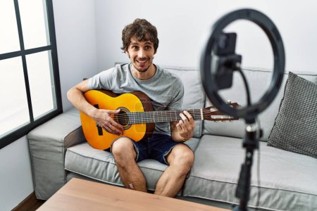 Téléchargez les photos : Jeune homme hispanique ayant concert en ligne jouer de la guitare classique à la maison - en image libre de droit