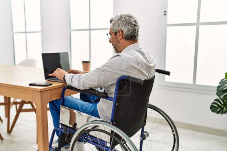 Téléchargez les photos : Homme d'affaires aux cheveux gris d'âge moyen assis en fauteuil roulant et travaillant au bureau - en image libre de droit