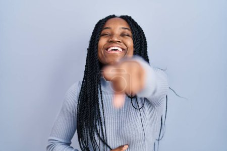 Foto de Mujer afroamericana de pie sobre fondo azul riéndose de ti, señalando con el dedo a la cámara con la mano sobre el cuerpo, expresión de vergüenza - Imagen libre de derechos