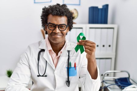 Photo for African doctor man holding support green ribbon looking positive and happy standing and smiling with a confident smile showing teeth - Royalty Free Image
