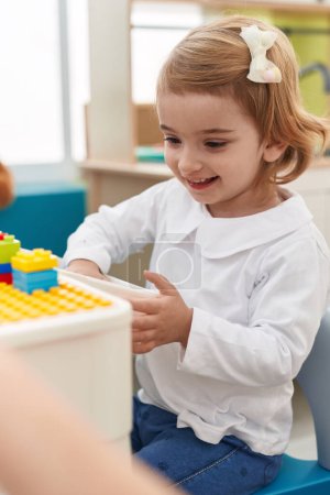 Foto de Adorable chica caucásica jugando con bloques de construcción sentado en la mesa en el jardín de infantes - Imagen libre de derechos