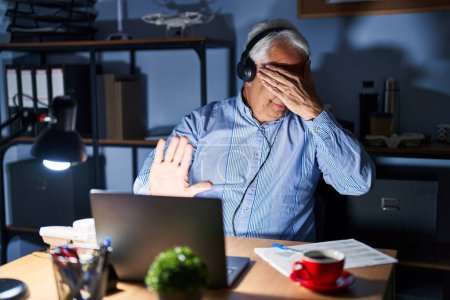 Photo for Hispanic senior man wearing call center agent headset at night covering eyes with hands and doing stop gesture with sad and fear expression. embarrassed and negative concept. - Royalty Free Image