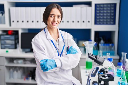 Photo for Young beautiful hispanic woman scientist smiling confident sitting with arms crossed gesture at laboratory - Royalty Free Image