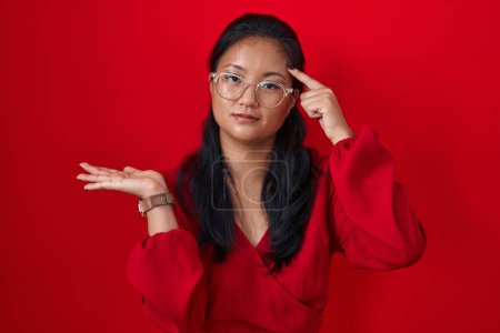 Téléchargez les photos : Asian young woman standing over red background confused and annoyed with open palm showing copy space and pointing finger to forehead. think about it. - en image libre de droit