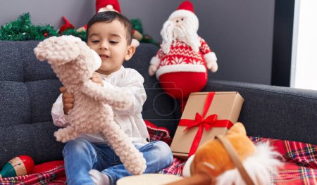 Photo for Adorable hispanic toddler playing with toys sitting on sofa by christmas decor at home - Royalty Free Image