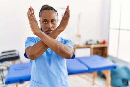 Foto de Mujer negra con trenzas trabajando en la clínica de recuperación del dolor expresión de rechazo cruzando brazos haciendo signo negativo, cara enojada - Imagen libre de derechos